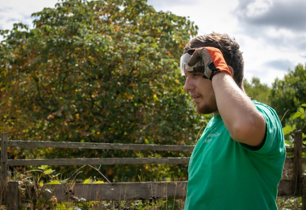 A person is showing raising safety goggles from their eyes in a garden setting