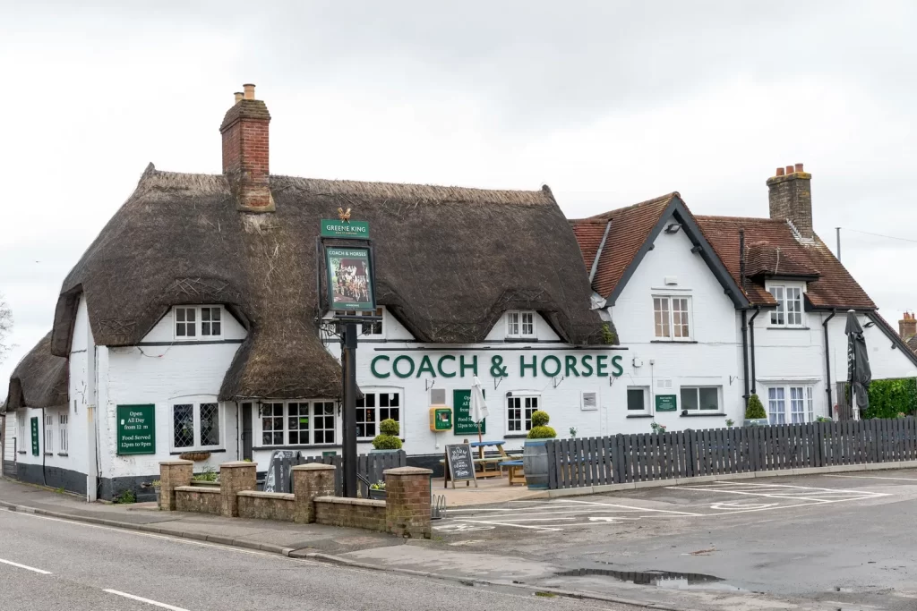 a pub with a thatched roof - it is visible from the front, outside in a wide shot.